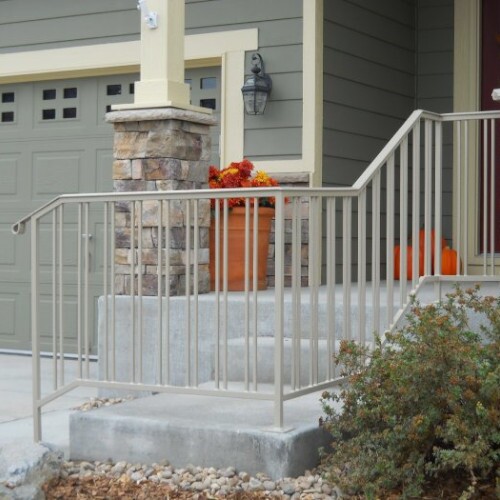 A light grey steel railing on concrete steps and a porch leading to the front door of a dark grey home with light yellow trim.