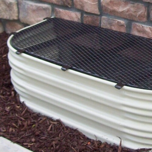 A black grate window well cover for a white window well surrounded by mulch against a red stone home.
