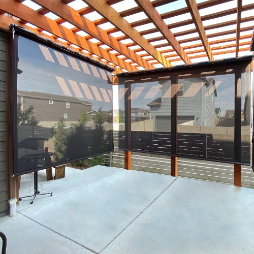 A wooden pergola covering a patio with a fire pit and seating area, stone pillars, and sun shades extending from one side.